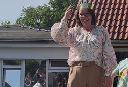 Frau mit Brille und Papierkrone lächelt vor einem Haus mit rotem Ziegeldach