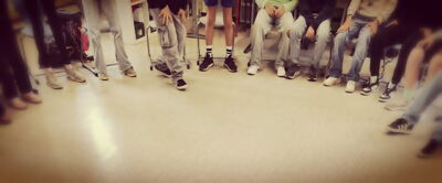 Gruppe von Menschen sitzt und steht im Kreis auf einem hellen Boden