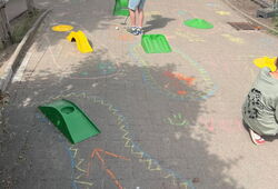 Kinder spielen Minigolf auf einem mit bunter Kreide bemalten Gehweg mit kleinen Hindernissen aus Kunststoff