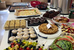 Buffet mit verschiedenen Kuchen, Muffins, Obstspießen und Getränkebehältern in einem hellen Raum