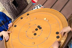 Kinder spielen an einem runden Holztisch mit einem Spielbrett, auf dem schwarze und helle Spielsteine liegen
