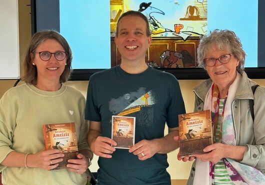 Matthias Kröner steht mit Katja Böttcher-Philipps und Luise Ehmke vor einer Leinwand, die ein Buchcover mit dem Titel 'Detektiv Ameisis' zeigt, und halten jeweils ein Exemplar dieses Buches in den Händen