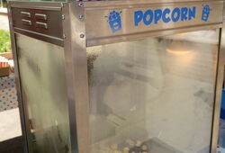 Popcornmaschine aus Edelstahl mit Popcorn und einer rot-weiß gestreiften Popcorntüte darauf unter bunten Wimpelketten