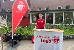 Person in rotem Poloshirt steht hinter einem Infostand mit der Aufschrift '1862' und dem Logo der Möllner Sportvereinigung neben einem roten Werbefahne mit der Webadresse 'www.moellnersv.de'