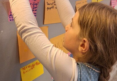Mädchen mit geflochtenem Haar klebt bunte Notizzettel an eine Wand