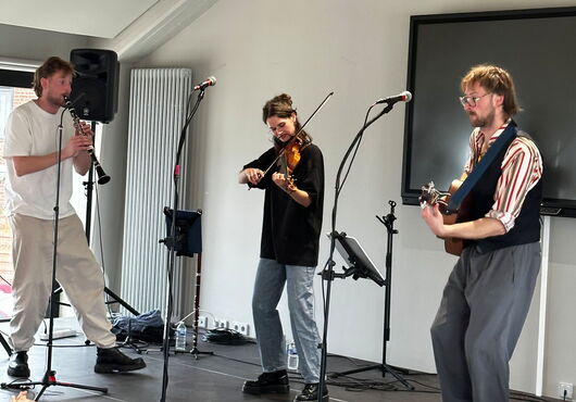 Drei Musiker auf einer Bühne spielen Klarinette, Geige und Gitarre