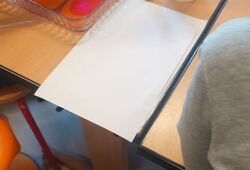 Mehrere Hände tauchen Papier in eine flache Schale mit buntem Wasser auf einem Tisch