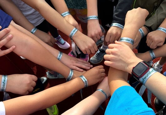 Gruppe von Menschen, die ihre Arme mit hellblauen Armbändern in die Mitte strecken