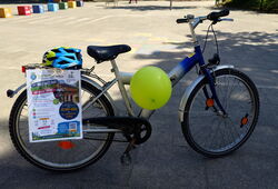 Jugendliches Fahrrad mit blauem Helm auf Gepäckträger und grünem Luftballon am Rahmen auf Asphalt stehend